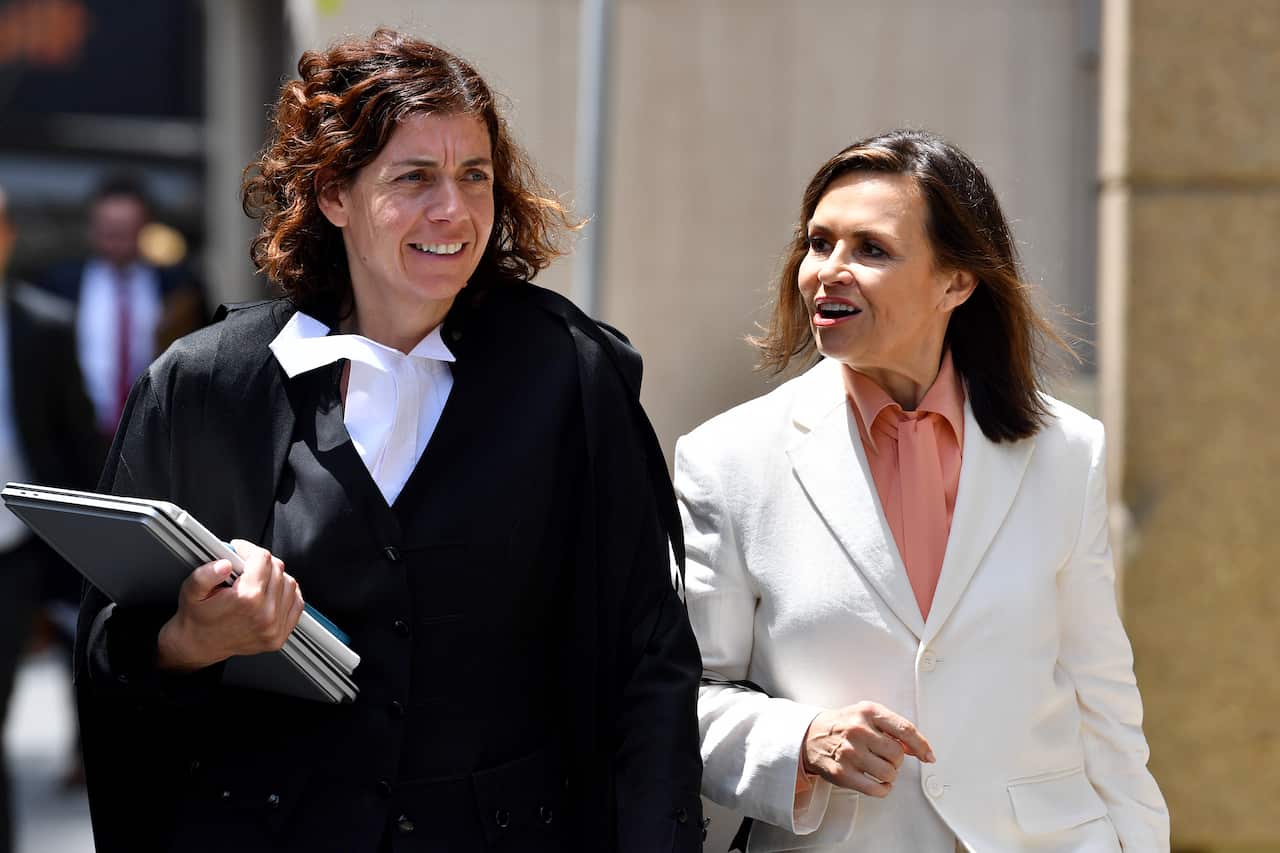 Two women wearing formal attire, one the gown and ruff of a barrister, talking while walking outside.