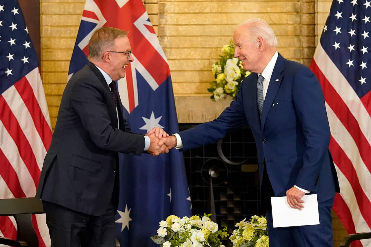 Two men in suits shaking hands with American and Australian flags in backround