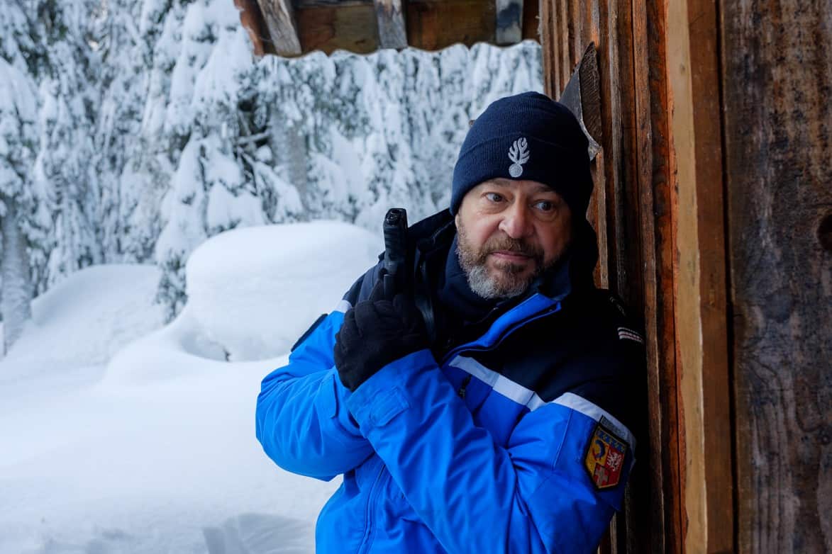 Policeman waits with a gun drawn outside a snowy cabin 