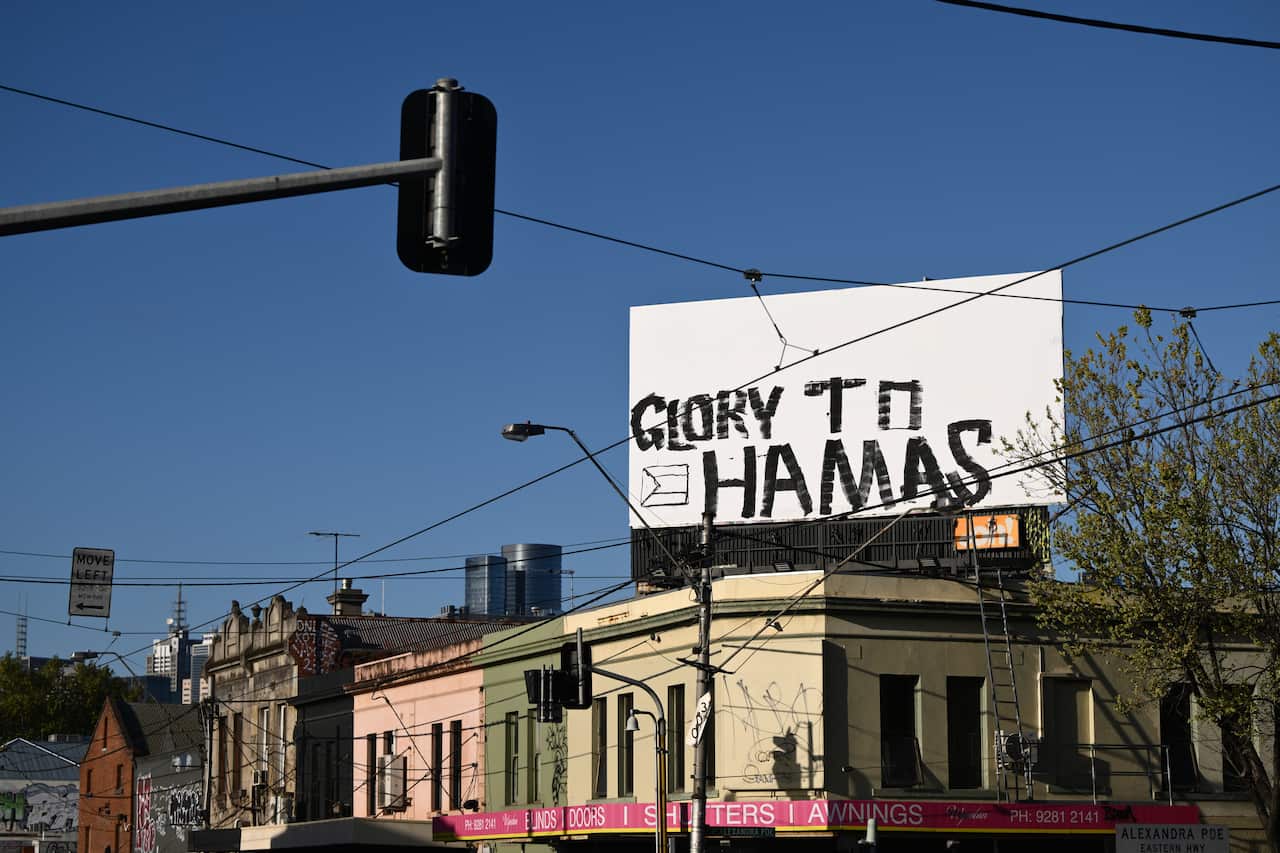 A white billboard above a group of buildings that has been graffitied with the words "Glory to Hamas".