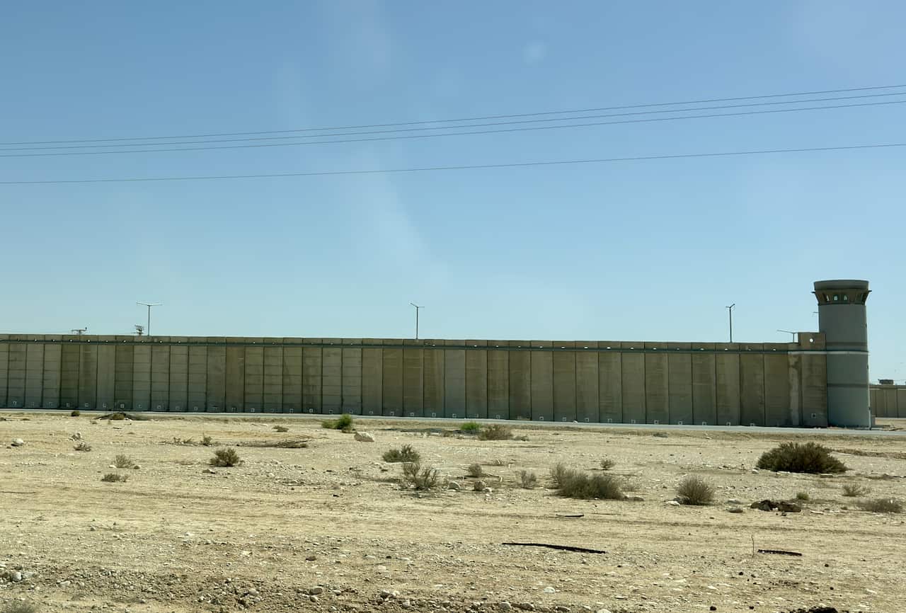 A wall along the desert, set against a light blue sky with sand in the foreground.