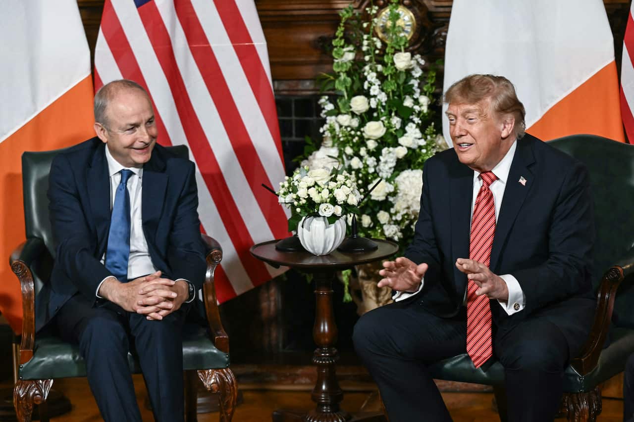 US President Donald Trump gestures while speaking during a seated meeting with Irish Prime Minister Micheál Martin, with American and Irish flags in the background.