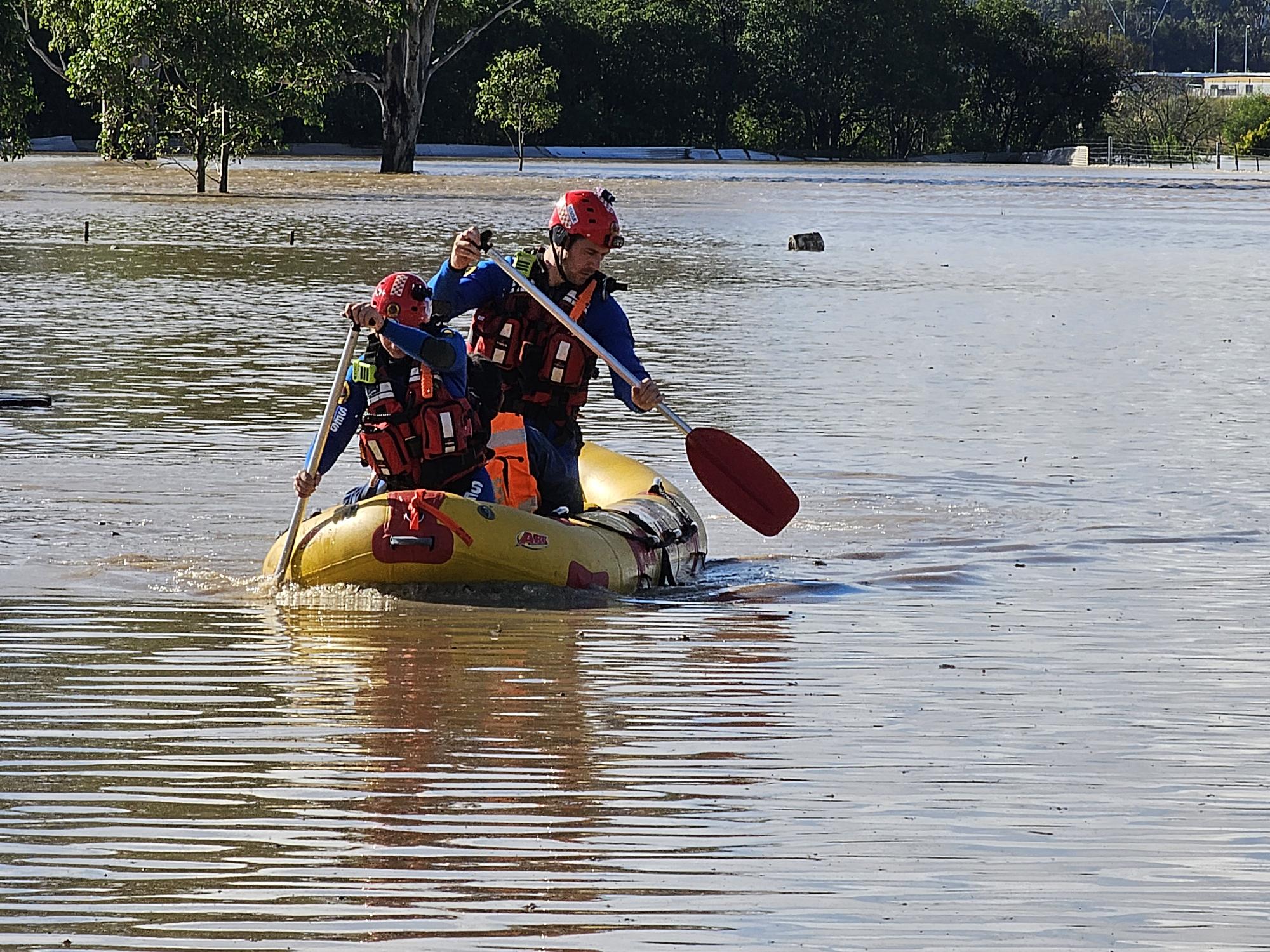 NSW SES workers paddle in a flooded river.
