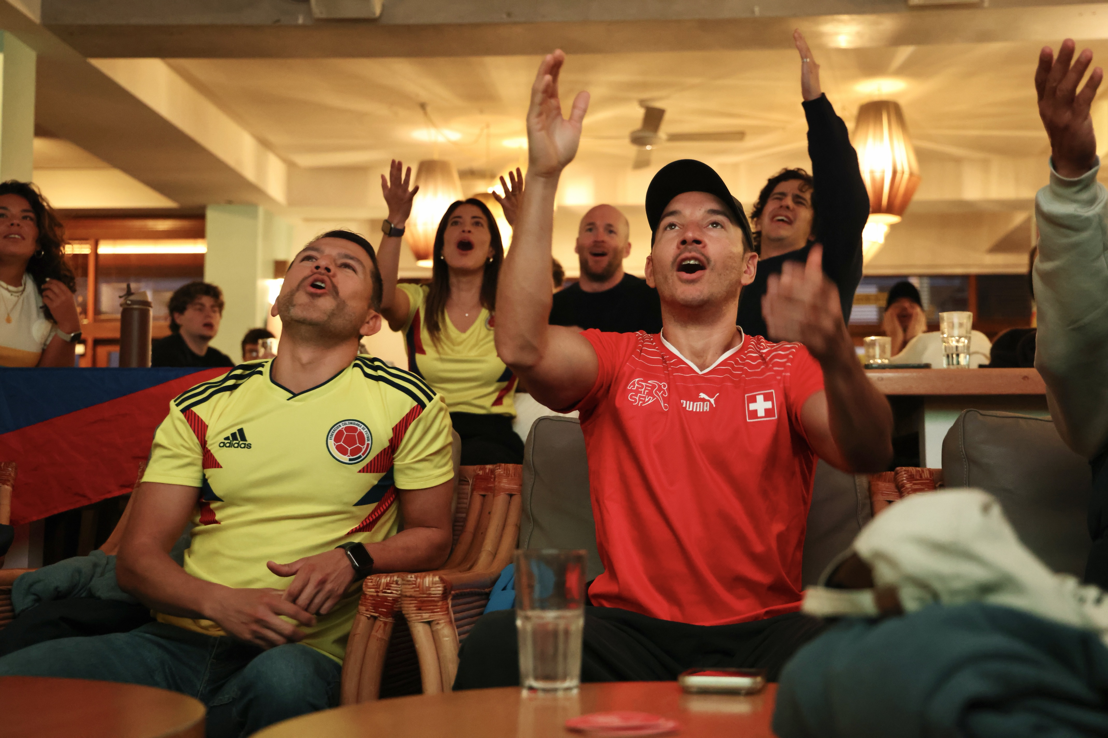 A group of football fans in red and yellow shirts react to a match in progress.