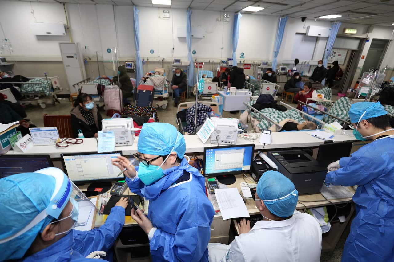 Staff in PPE behind a counter work while patients lay in beds in the background.
