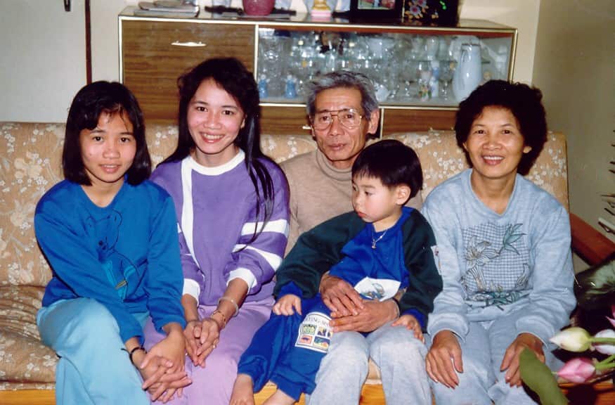 A Vietnamese family sitting on a sofa smiling at camera. 