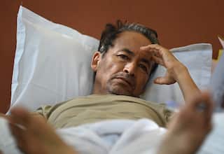 A man lies on a white pillow with his hand on his forehead