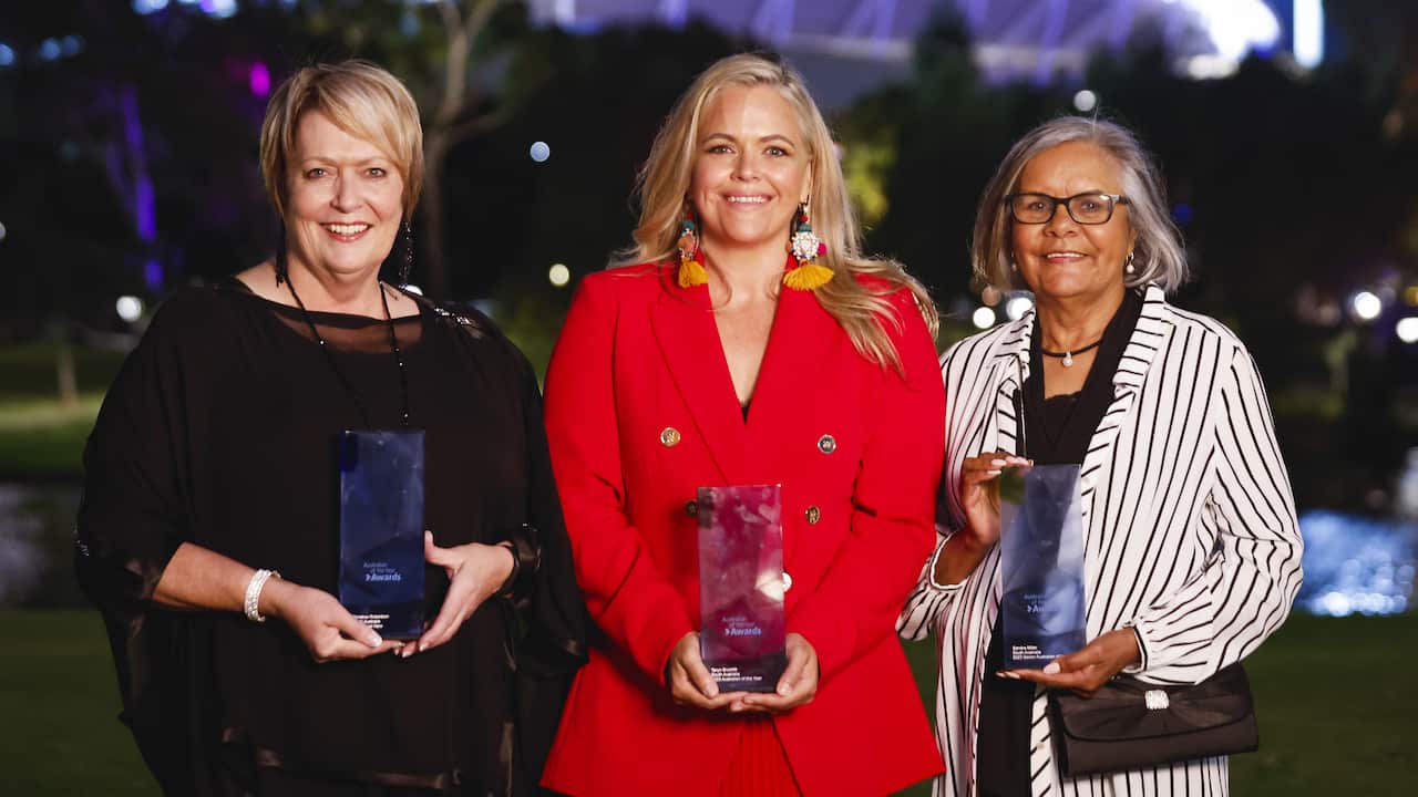 Three women smiling holding trophies
