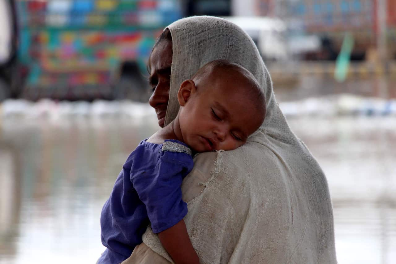 A mother holds a baby in front of flooded water. 