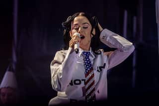 Katy Perry takes the stage in a stars and stripes tie and a white business shirt that says "I am not a robot" on it