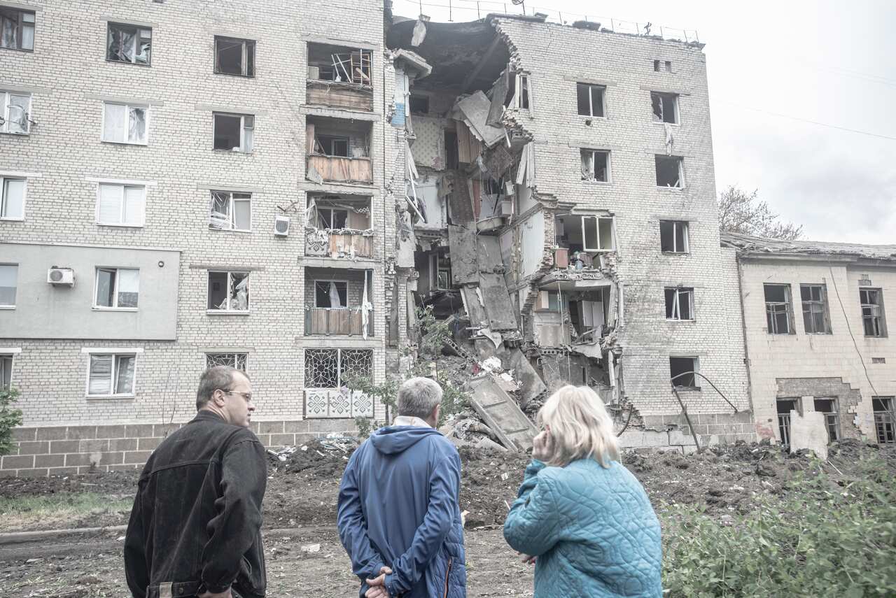 Three people looking at a destroyed residential building.