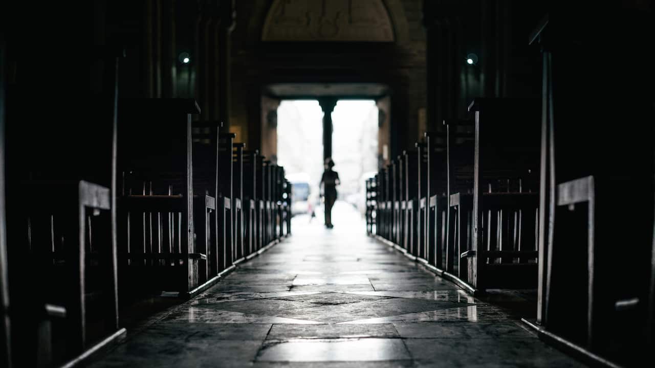Rows of bench inside a silent church with passerby moving in from exit