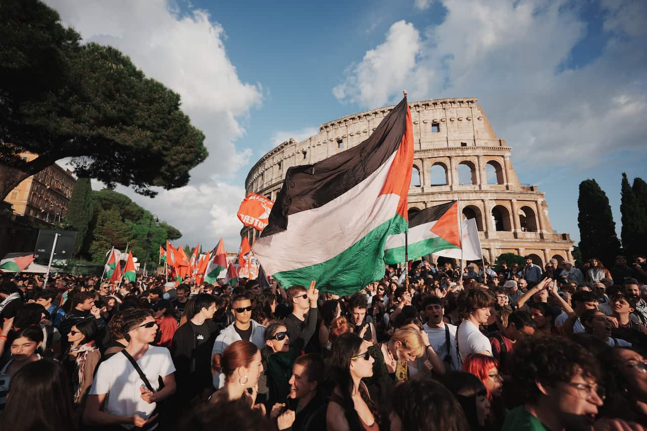 A crowd of people carrying Palestinian flags in front of the Colosseum in Rome.