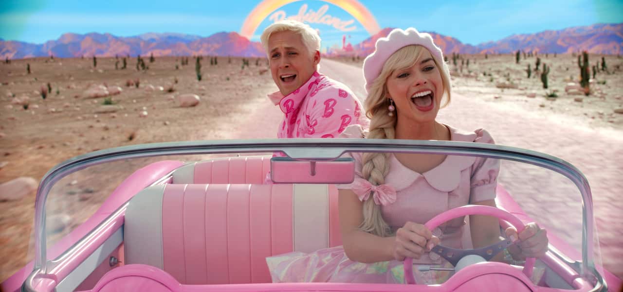 Barbie driving a pink convertible through the desert with Ken in the backseat