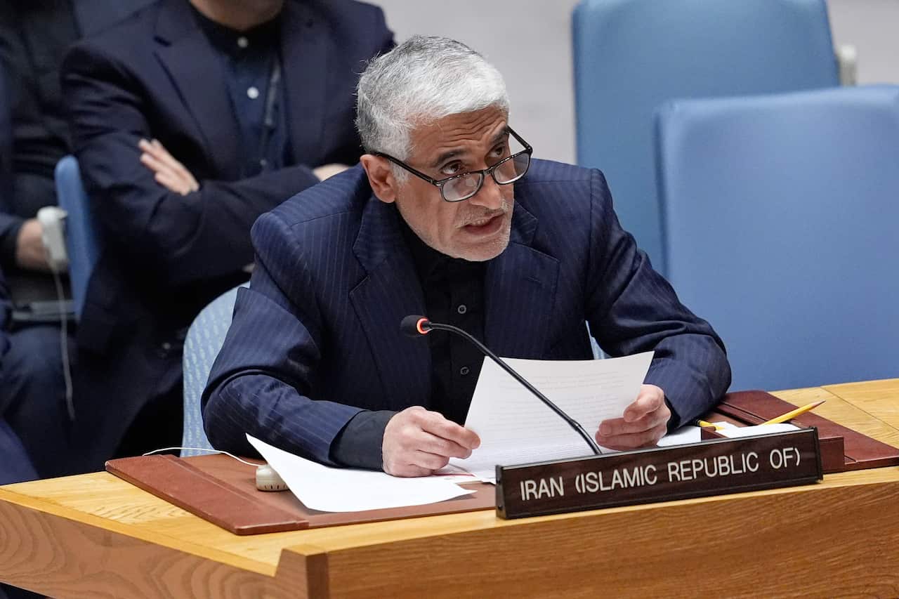 A man sitting at a desk, holding documents, with a plaque that reads "Iran (Islamic Republic of)"
