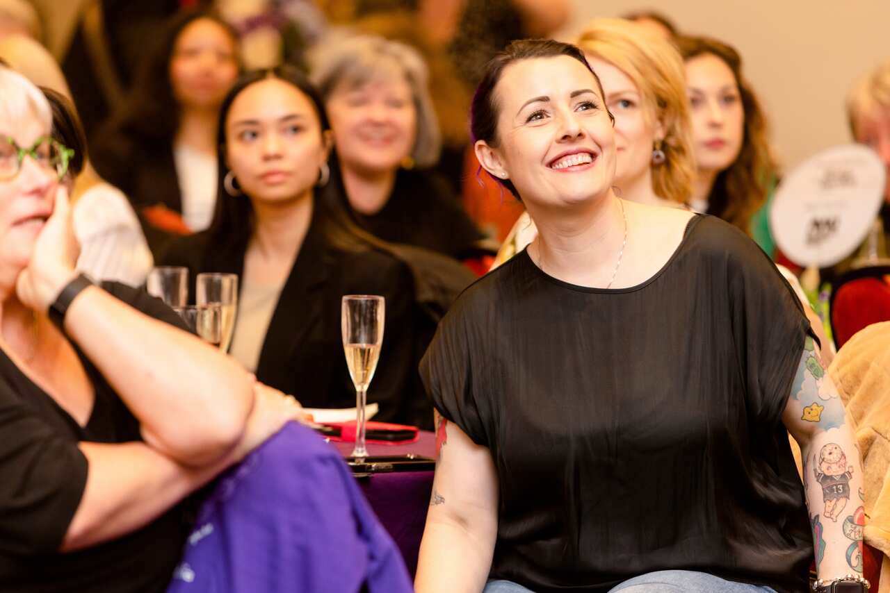 A woman wearing a black shirt sitting at a table at an event.