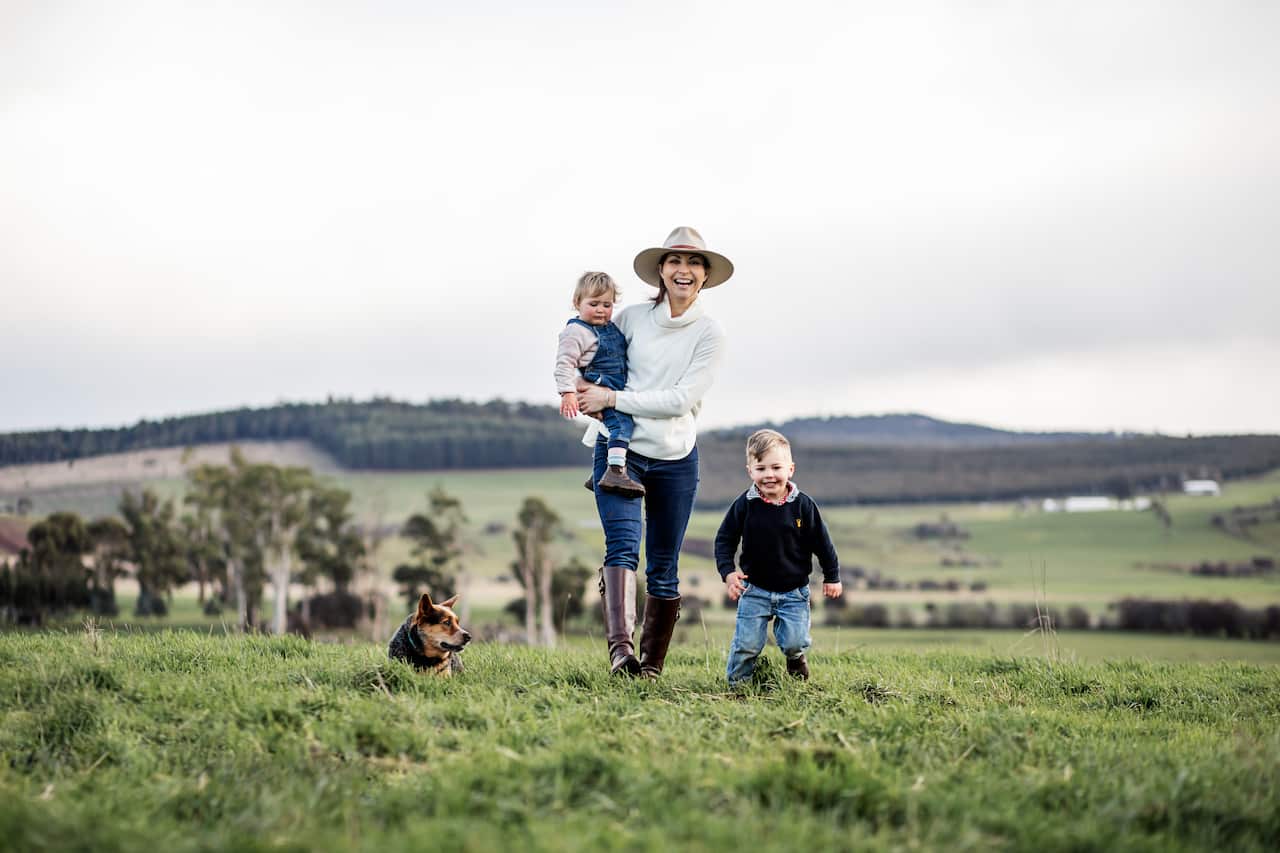 A woman with two young children and a dog outside on a farm.