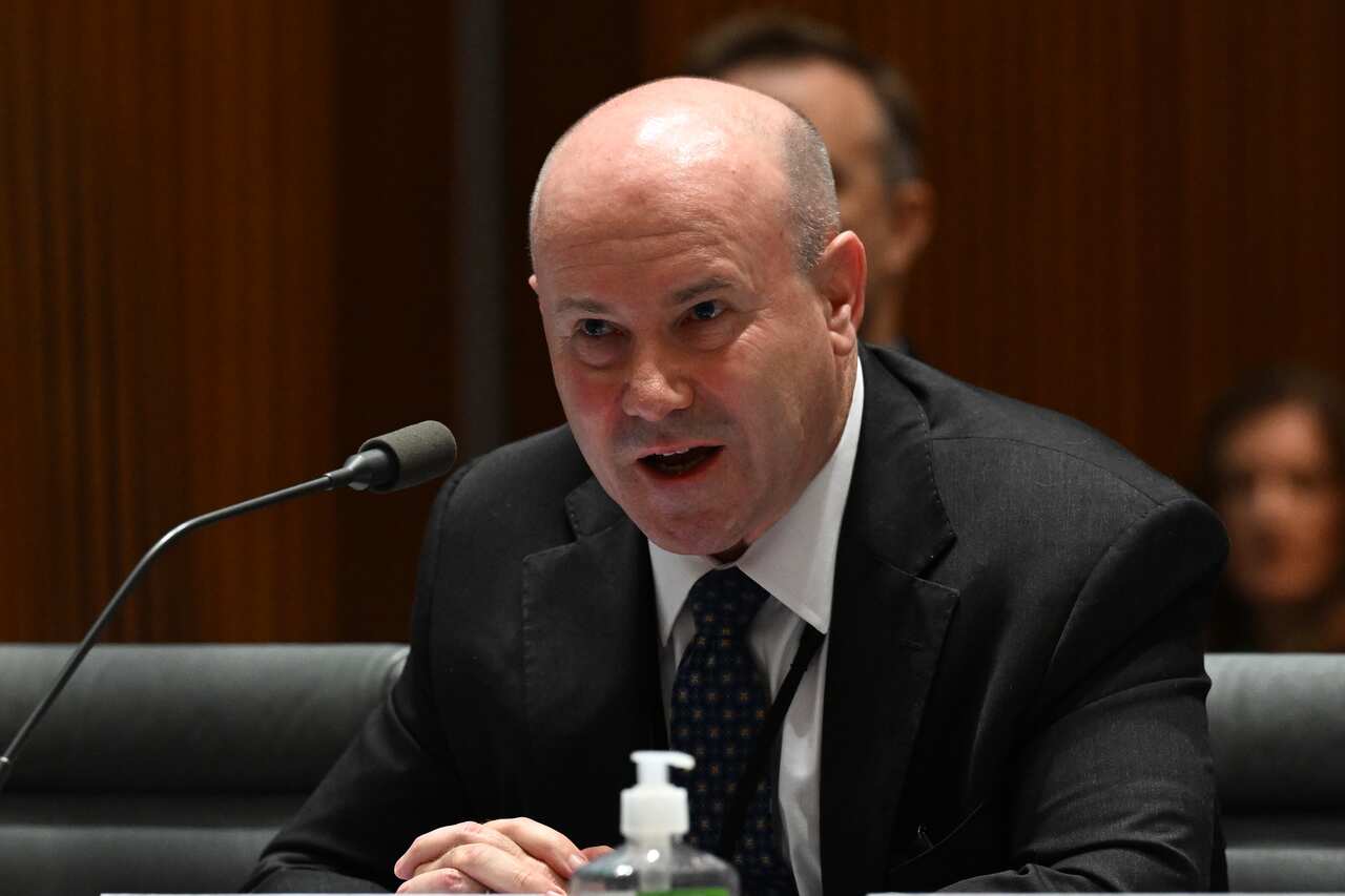 A man in a dark suit sitting and speaking into a microphone