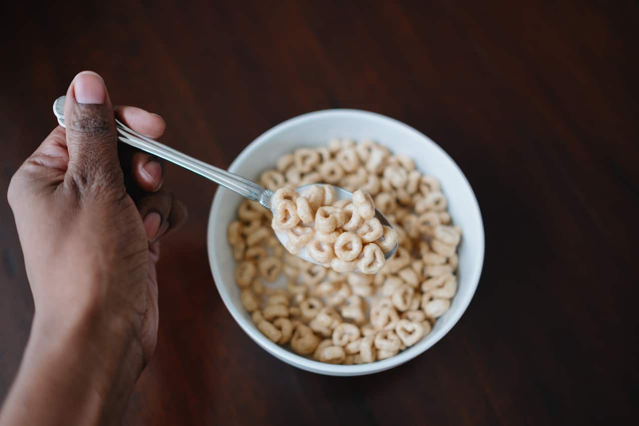 A hand holds a spoonful of cereal above a bowl filled with cereal and milk.