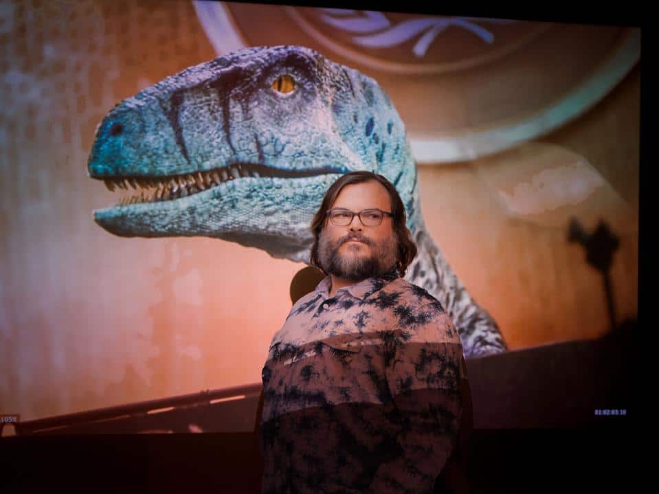 Actor Jack Black in front of a screen showing an image of a dinosaur