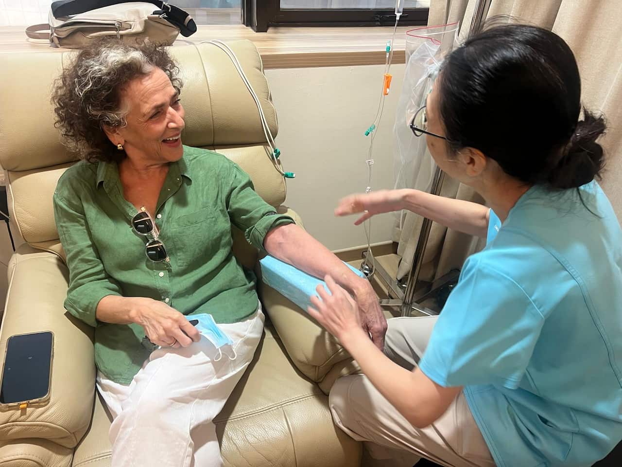 A woman smiles as she sits in a chair and receives medical treatment by a clinician.