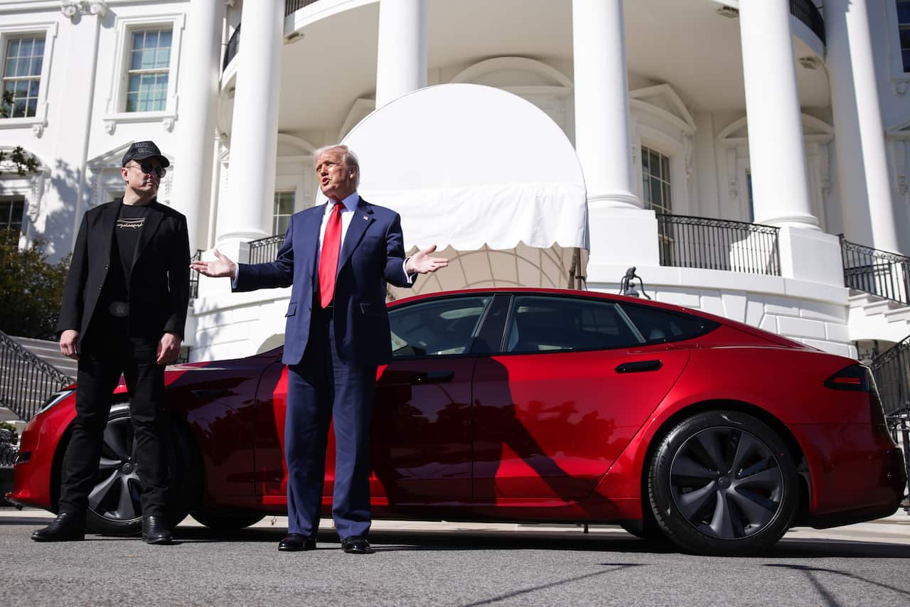 Two men standing beside a red vehicle.