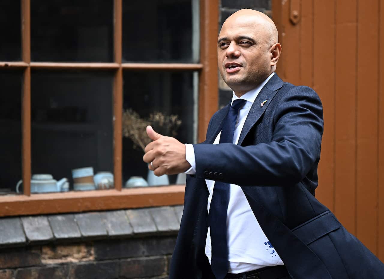 Sajid Javid walks along the street, moving his left hand forward in a potential thumbs up sign.