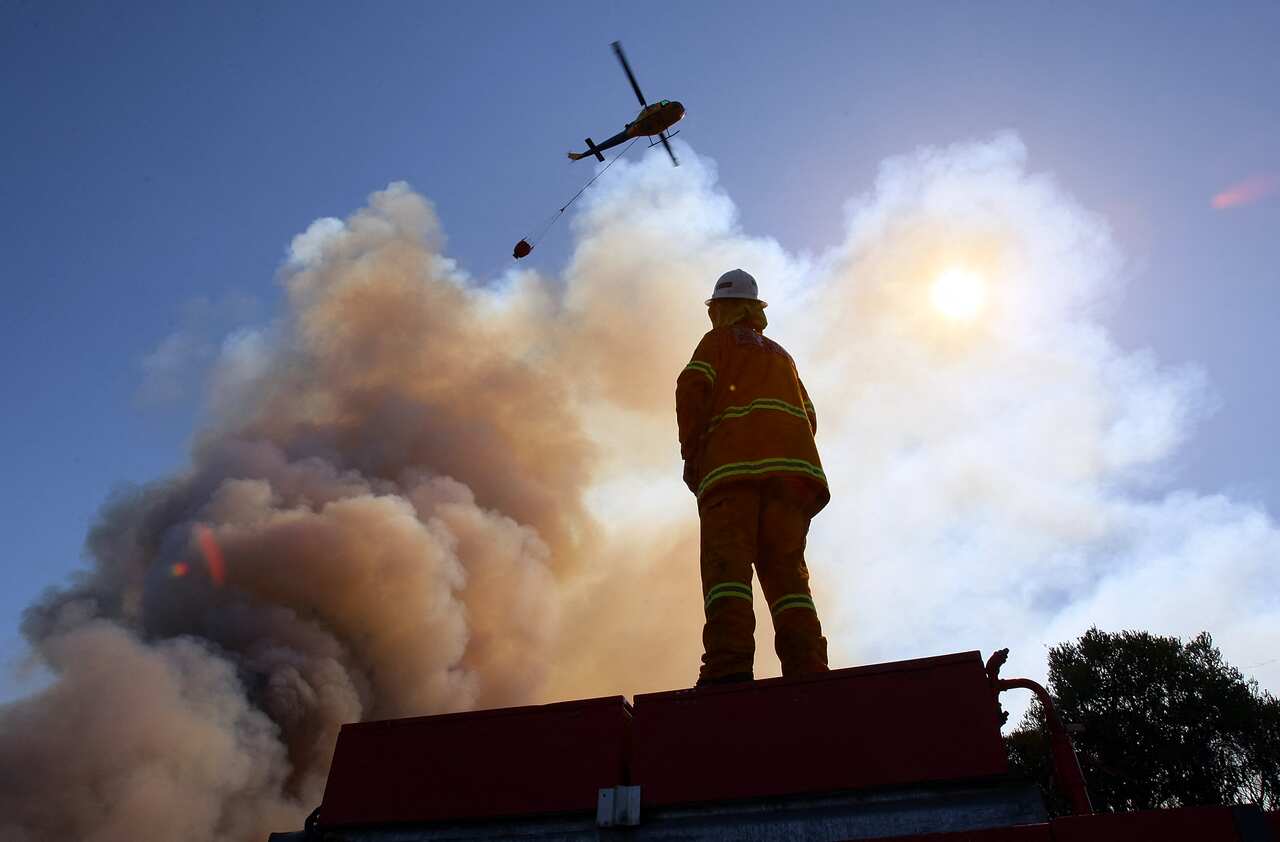 A firefighter standing watching a helicopter drop water on a firey cloud.