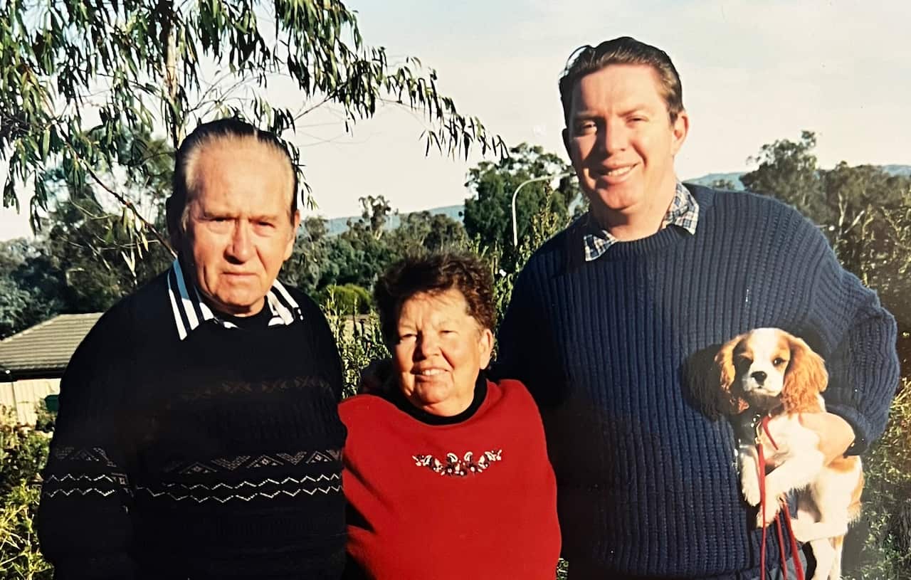 Three adults stand outside for a family photo. One is holding a puppy.