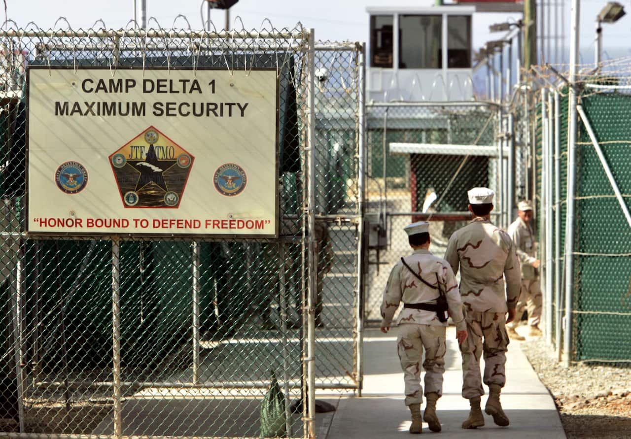 Two soldiers walk into a heavily fortified prison with high fences covered in barbed wire