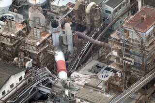 A collection of old buildings, through which a large smokestack has fallen, crushing several rooftops.