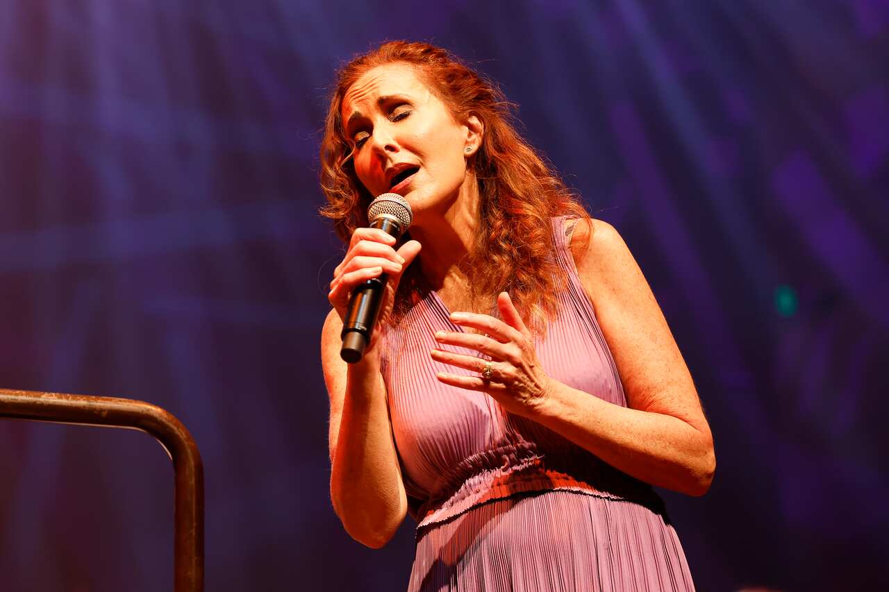 A woman with red hair sings into a microphone with her eyes closed.