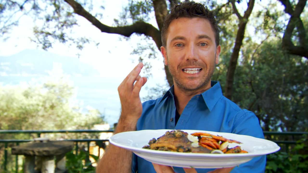 A smiling man in a blue shirt holds a plate of food.