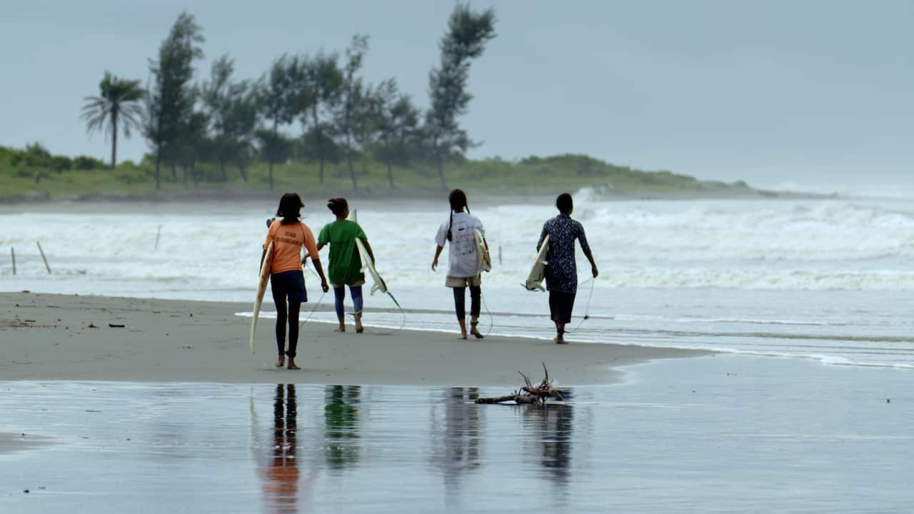 Four people carrying surfboards.