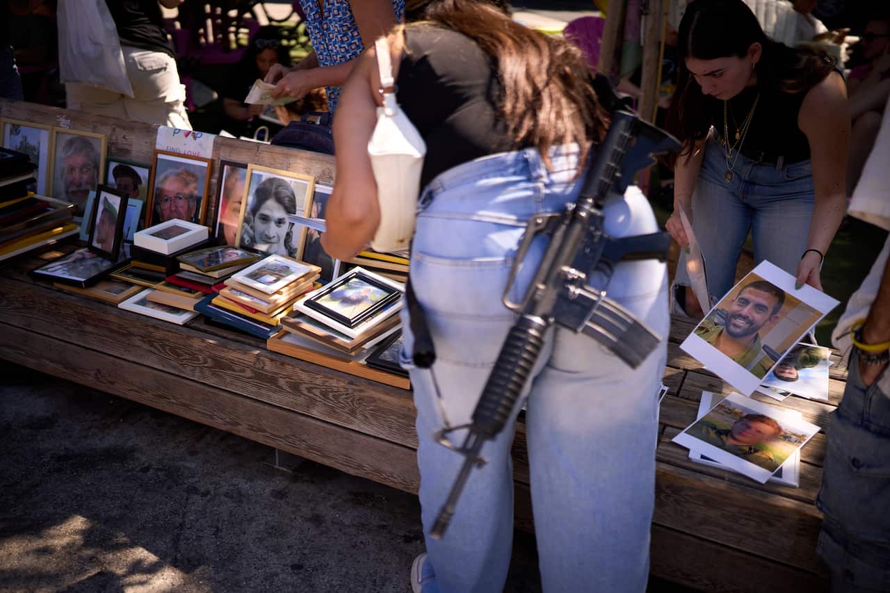 A woman carrying a rifle places images at a memorial for victims of the October 7 attack.