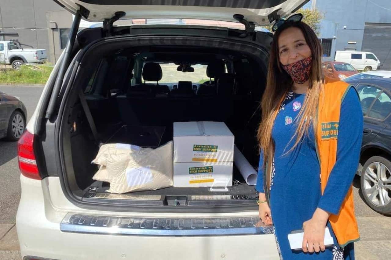 A woman with a face mask on, poses next to a car.