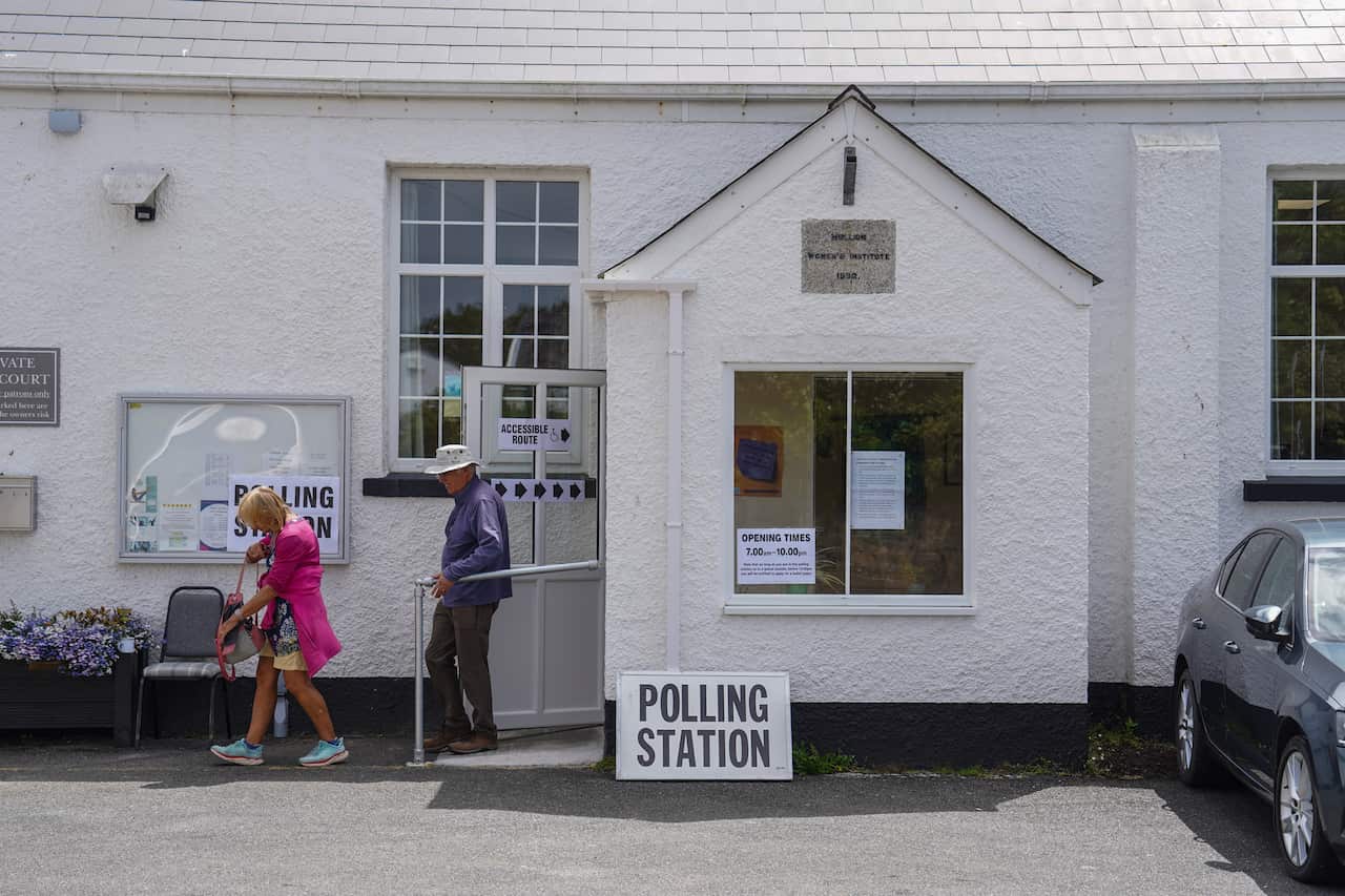 Two people walk out of a building with 'polling station' signs out front 