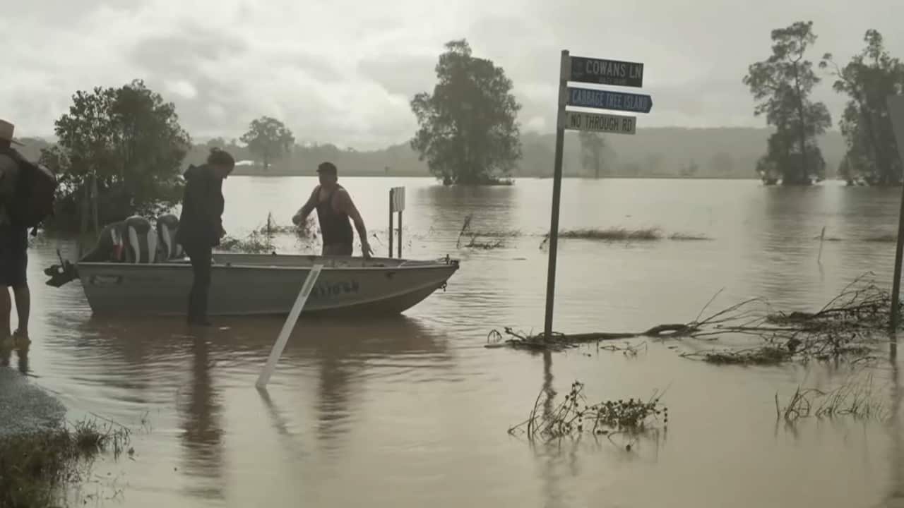 A small tinny boat with motor sitting on floodwaters, the street sign about a third underwater, with trees in the background clearly showing the high level of the widespread flood water.