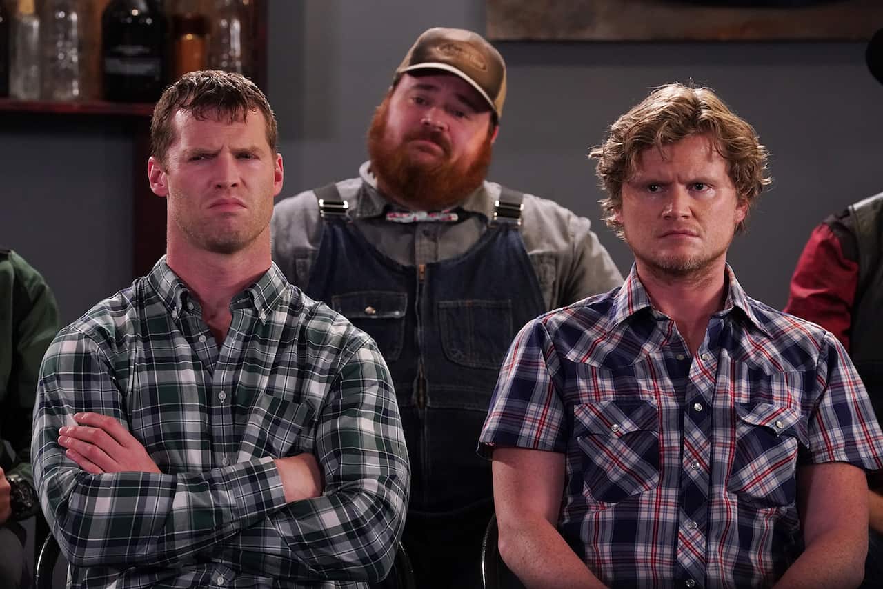 Three men stand close together, with puzzled expressions. 