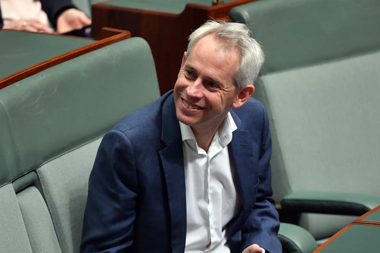 A white man in a suit smiles while sitting in parliament