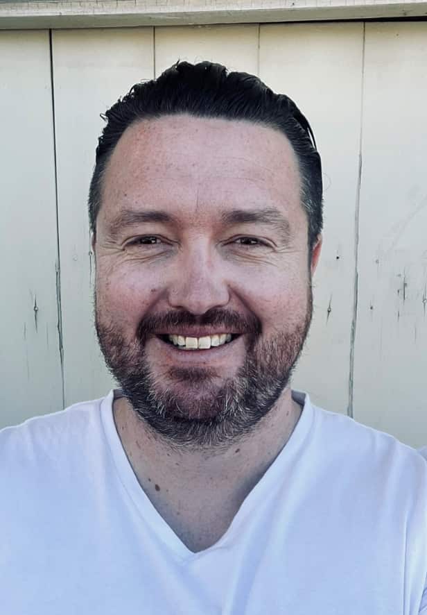 A bearded man in a white shirt smiles.