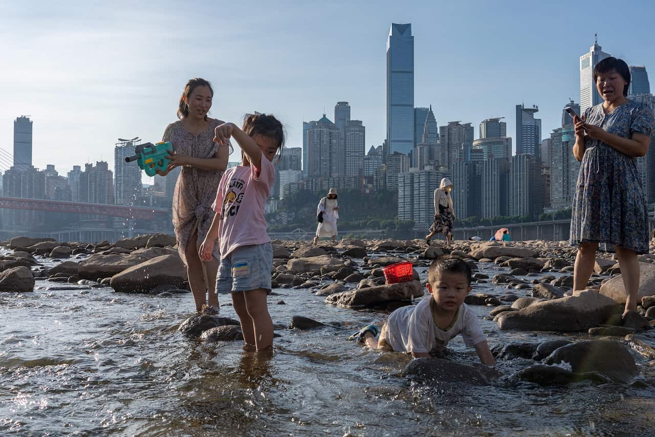 A woman and two children in low-lying water with city buildings in the background.