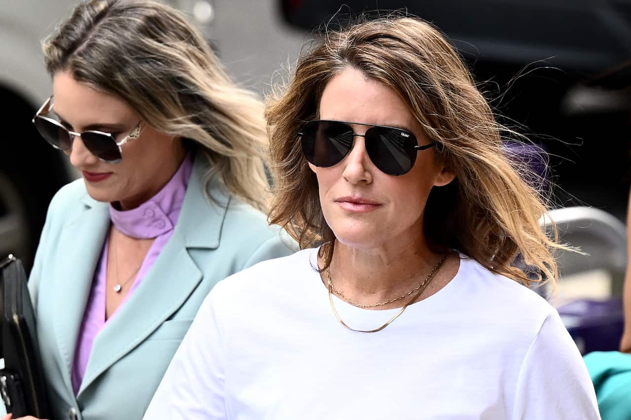 A woman wearing sunglasses and a white top. There is a woman wearing sunglasses and a mint-coloured jacket just behind her