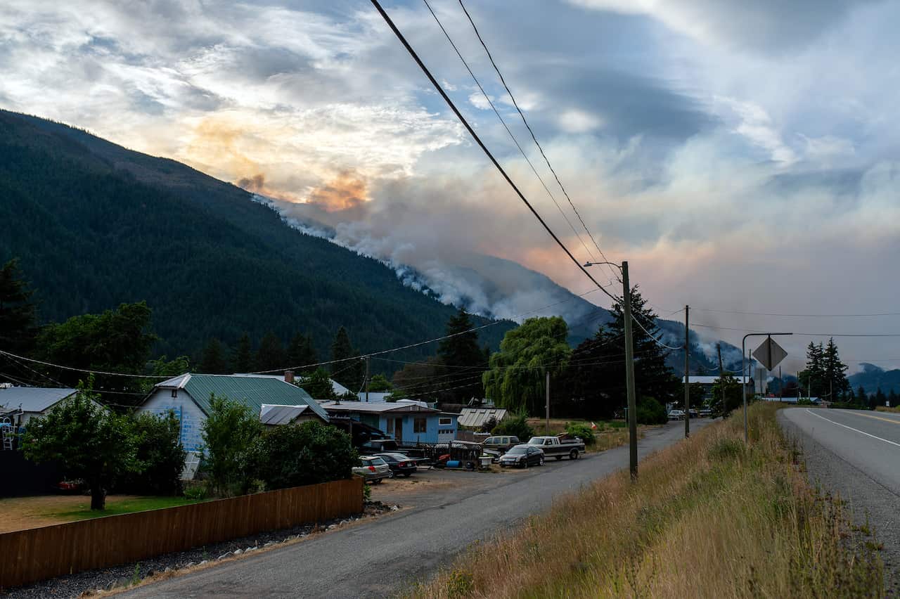 Houses along a road, with mountains in the distance and smoke rising from them.