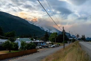 Houses along a road, with mountains in the distance and smoke rising from them.