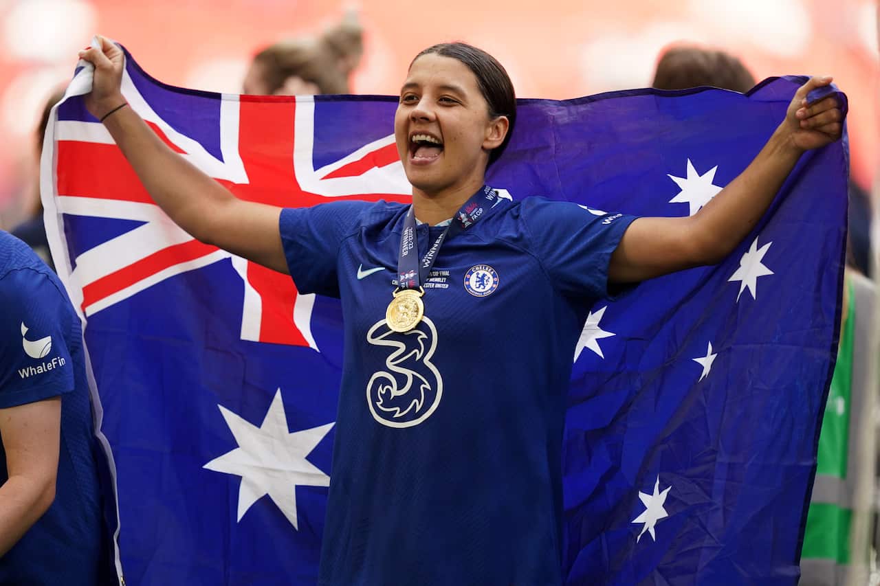 A woman in a flue football kit holding an Australian flag and wearing a champion's medal.