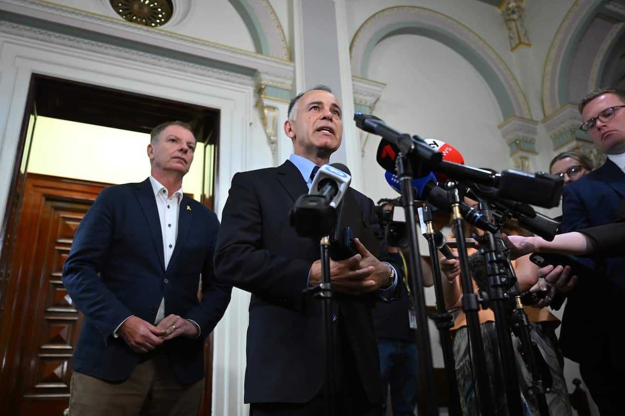 A man in a suit speaks at a press conference with another man standing behind him.
