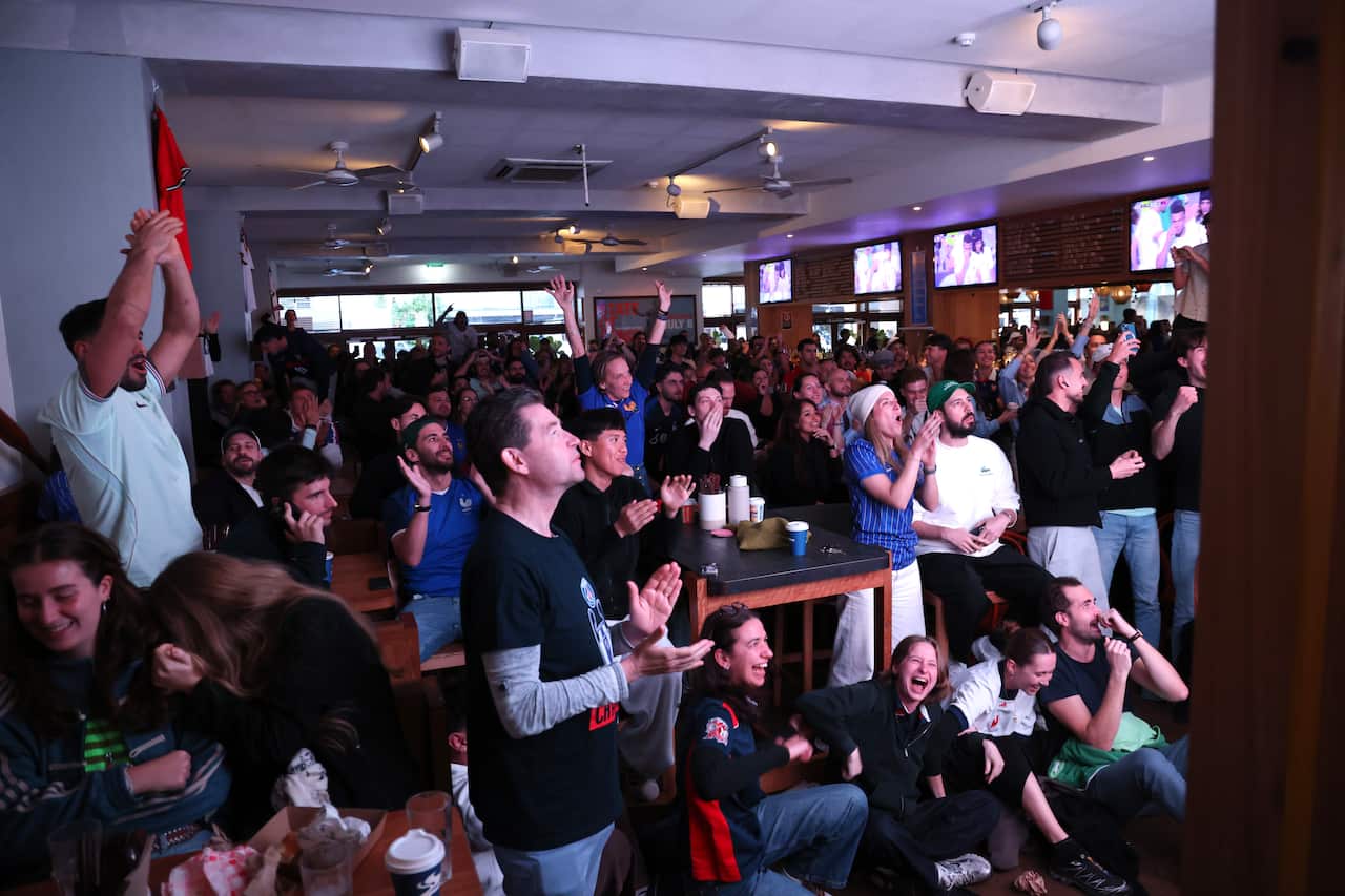 Dozens of French football fans with hands in the air in a packed pub.