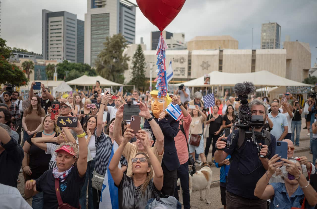 A group of people, some carrying Israeli and US flags, hold up their phones at an outdoor celebration.