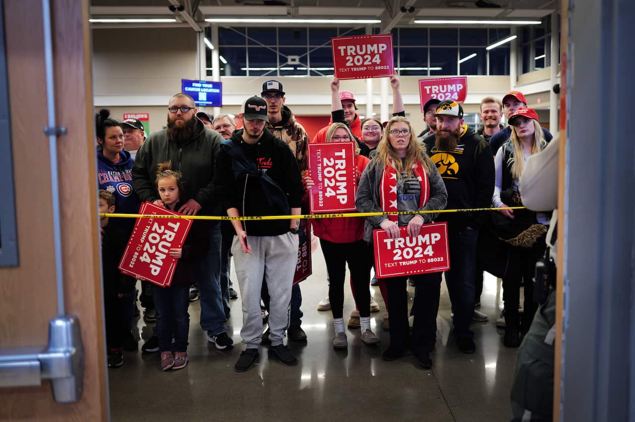 Donald Trump supporters holding campaign signs behind a yellow plastic tape. 
